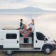 a couple sit on top of a self build campervan in front of the sea