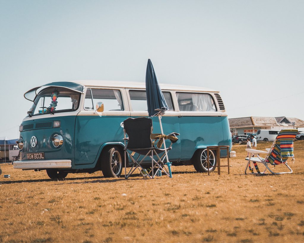 a blue VW camper is parked next to foldable chairs