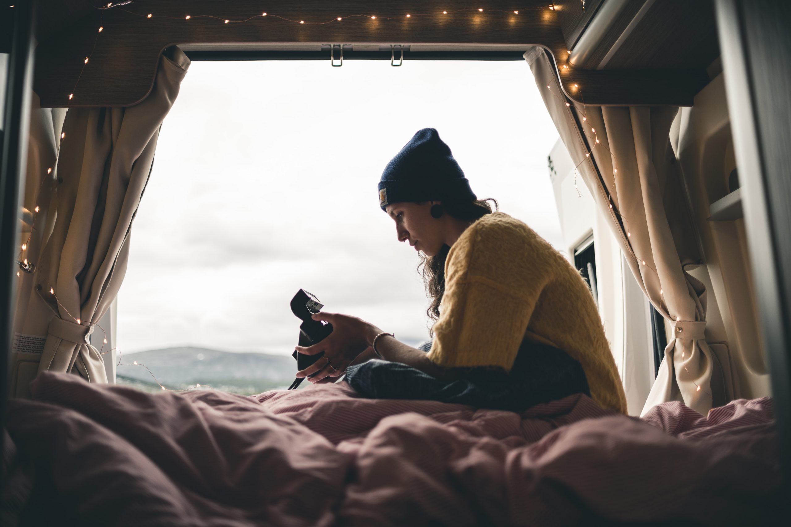 a woman sits on a bed of a converted campervan with the skyline behind her 
