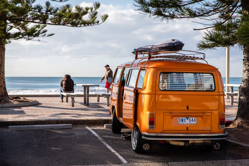 an orange campervan overlooks a beach scene 