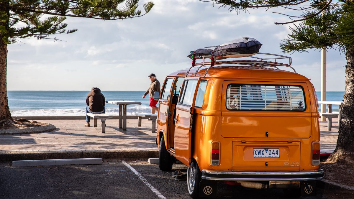 an orange campervan overlooks a beach scene