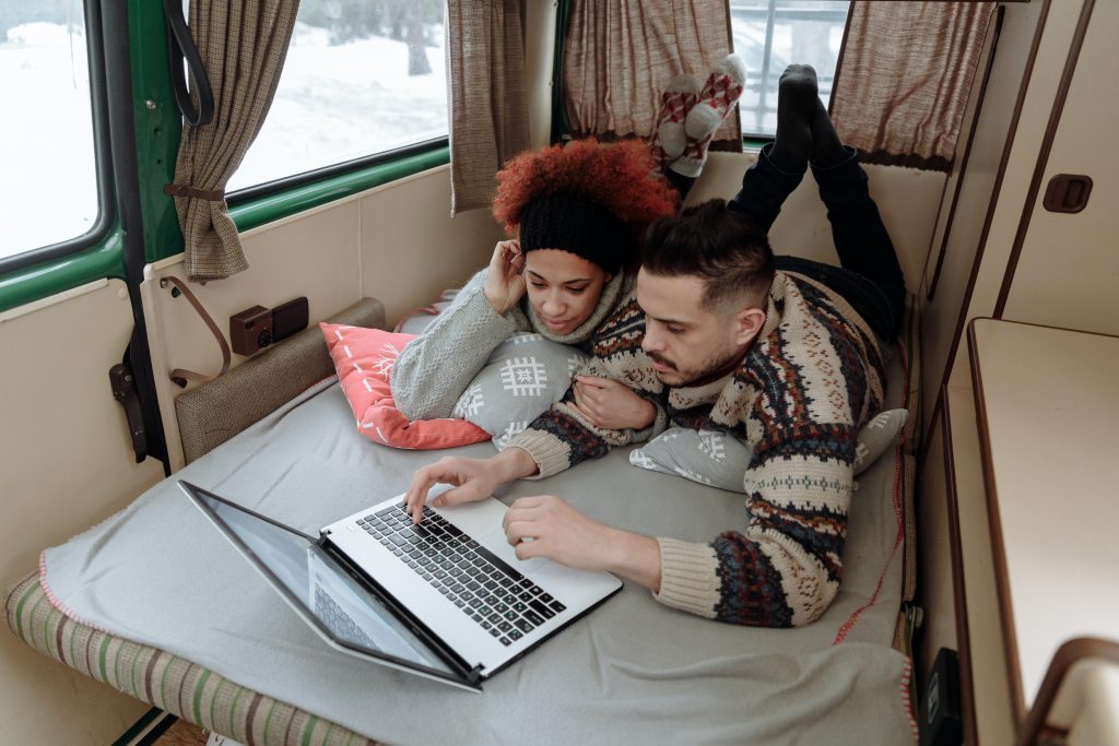 a young couple relax in a campervan while browsing the internet on a laptop