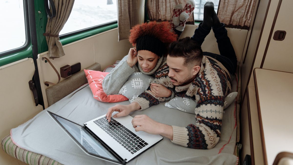 a young couple relax in a campervan while browsing the internet on a laptop