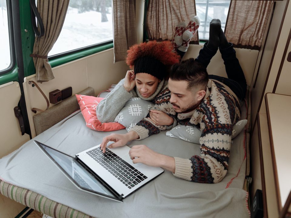a young couple relax in a campervan while browsing the internet on a laptop