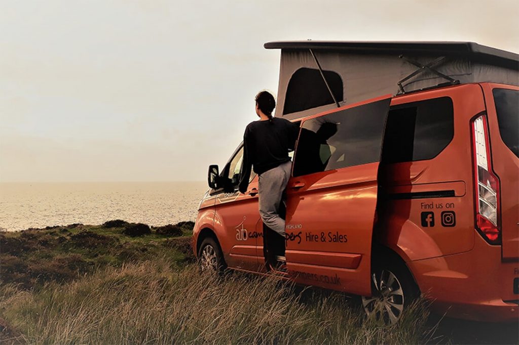 a woman leans out from a small orange campervan