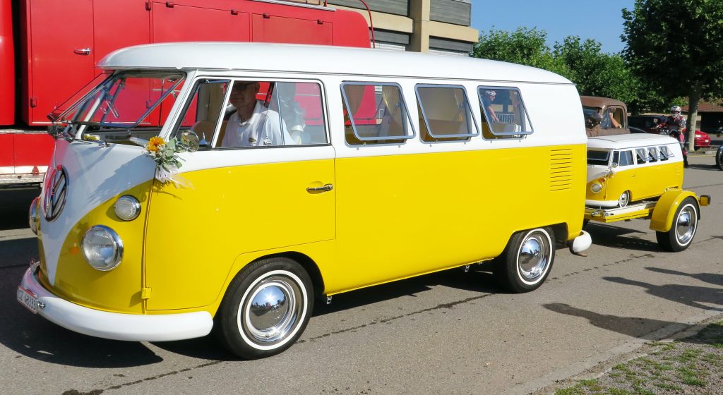 a bright yellow VW campervan with a trailer attached