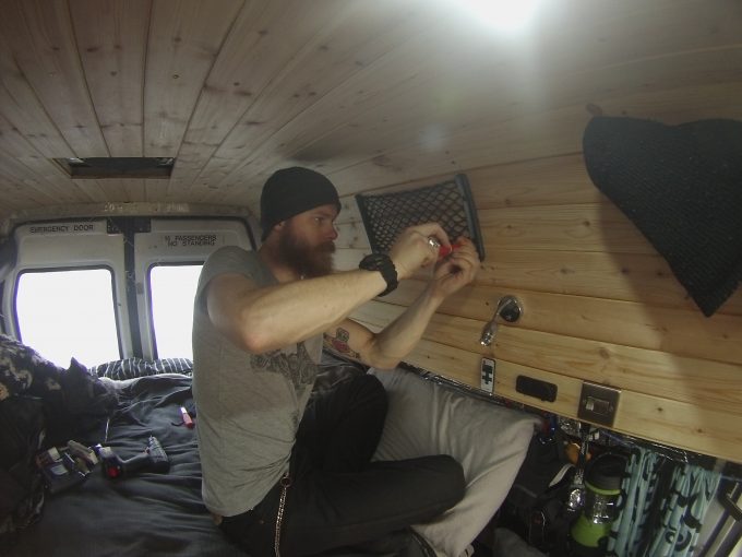 a man attaches storage nets to the inside of a converted camper
