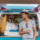 man leans on a blue converted campervan in the sunshine