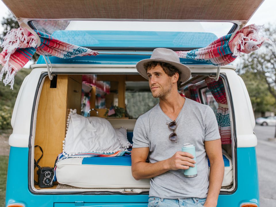 man leans on a blue converted campervan in the sunshine