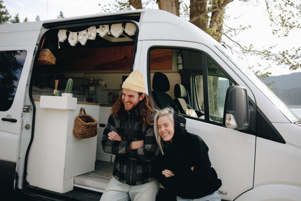 a couple leaning against a converted campervan laughing 